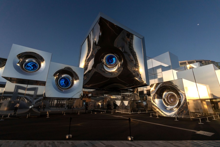 The exterior of an exhibition hall, dominated by large metallic cubes with deep circular insets.