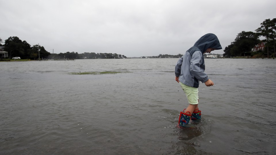 A boy wearing rainboots wades through the ankle-high water in Norfolk, Virginia.