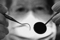 A black-and-white photo of a dentist wearing a face mask and holding up tools