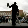 Al Norman, seen in silhouette, holds flyers and speaks to a crowd from a stage.