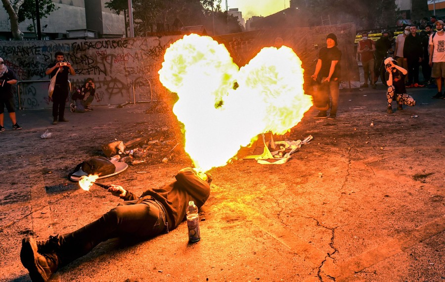 A person lies on their back on the ground, spitting flames upward, as several others watch.