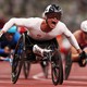 Several men in wheelchairs cross the finish line on a racetrack.