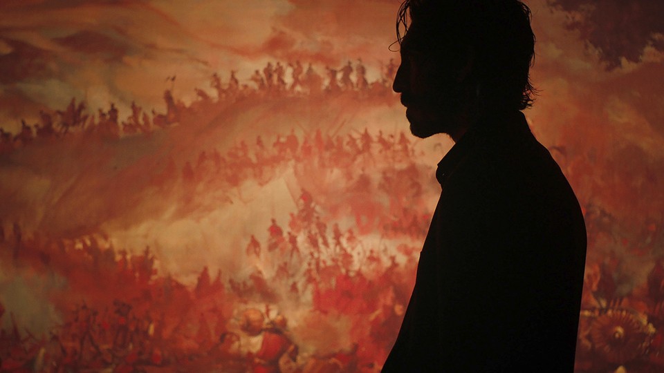 The character Kid in silhouette against an image of a battle in a scene from the film "Monkey Man"