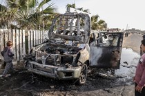 A burned shell of a car bearing World Central Kitchen logos sits along the side of a road as onlookers gather around it. The vehicle was damaged in an Israeli attack in Deir al-Balah, Gaza, on April 2, 2024. Seven staff members of the humanitarian organization, including Western nationals participating in food relief efforts and a Palestinian, were killed.