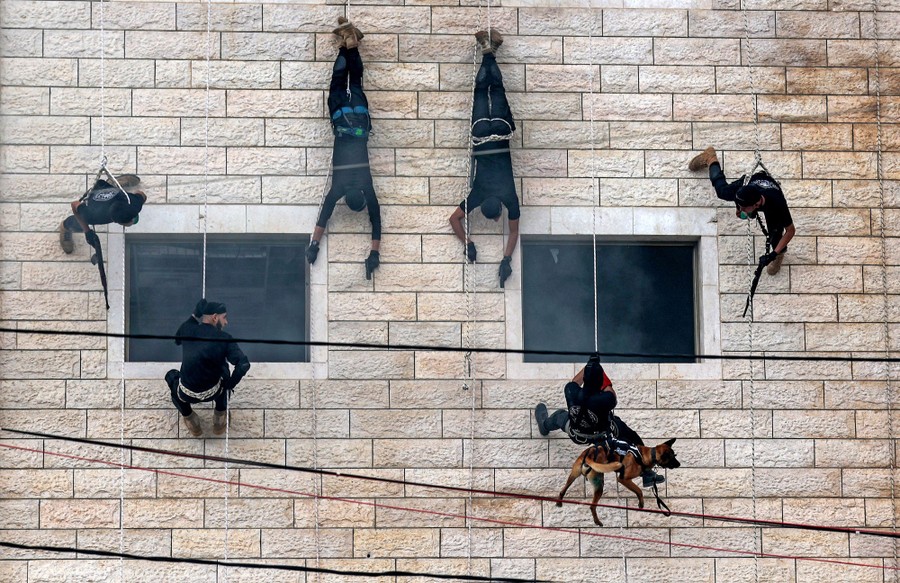 Six police graduates rappel down a wall.