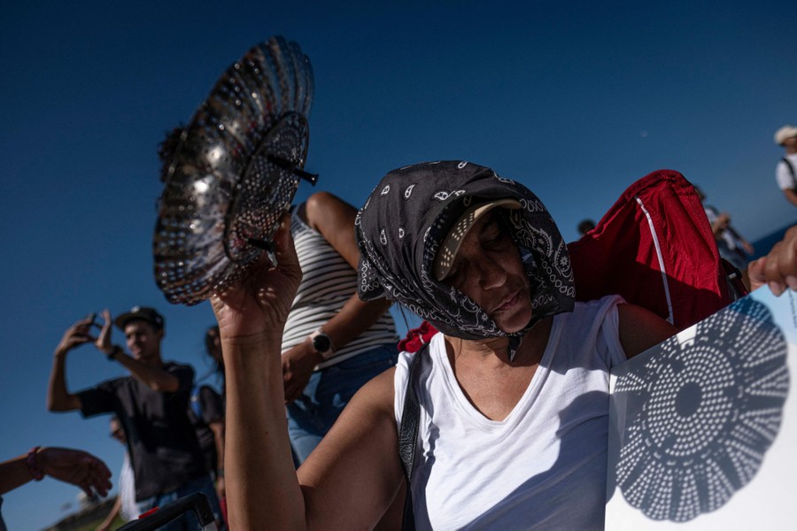 A person holds up a collapsible steamer basket, casting a shadow to view the eclipse through its many holes.