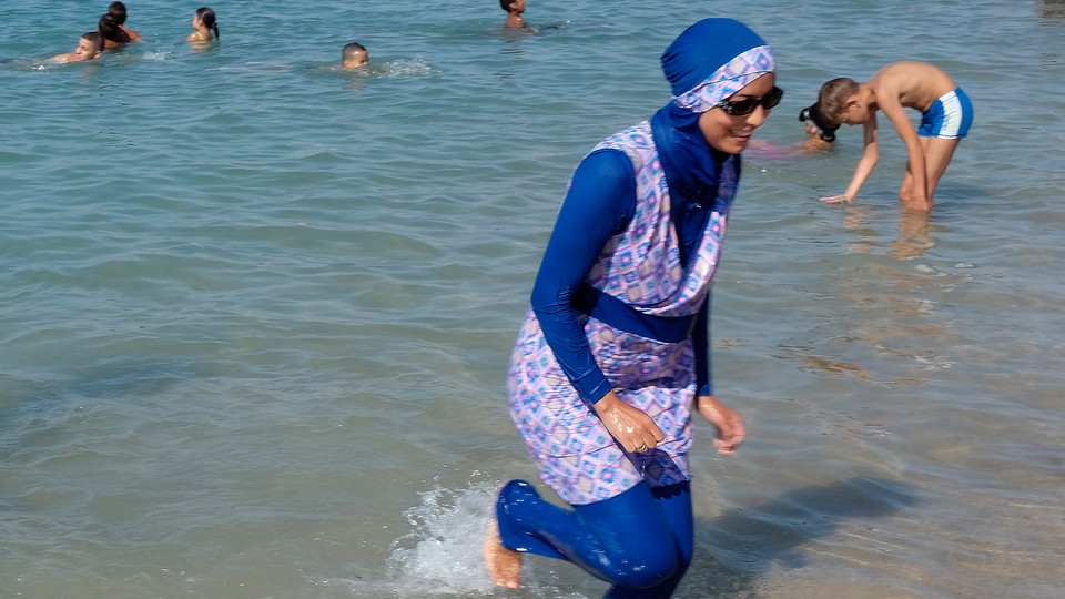 A woman wearing a burqini walks in the water on a beach in France.