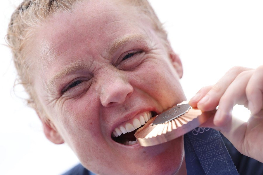 An athlete looks toward the camera while playfully biting a large bronze medal.