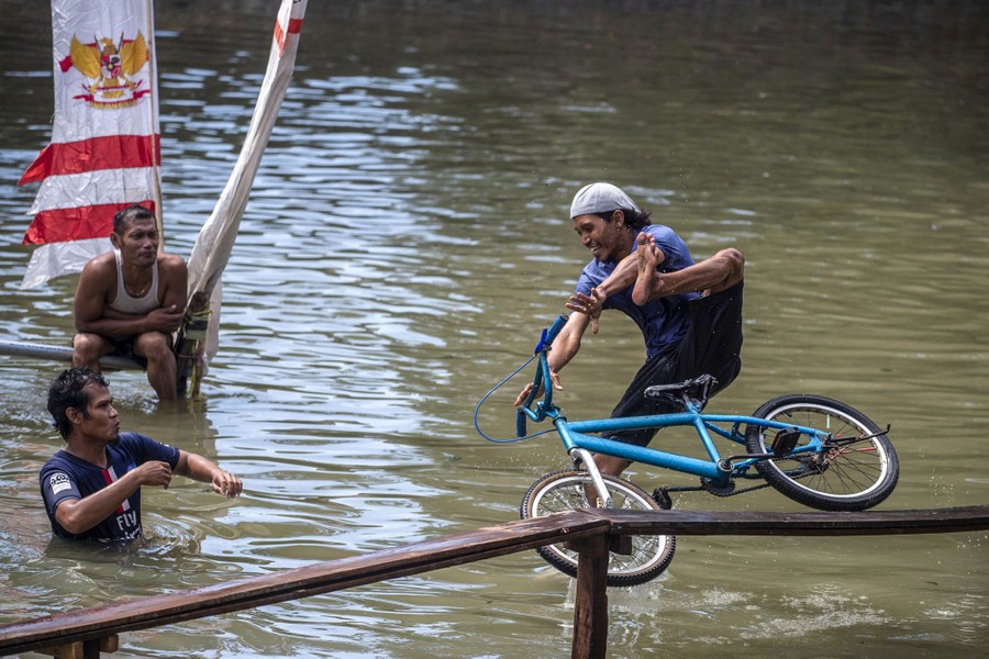 A person falls from a bike they were attempting to ride on a narrow plank above a body of water.