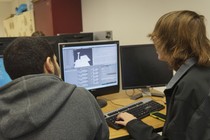 Taken from behind them, two young men stare at a computer screen