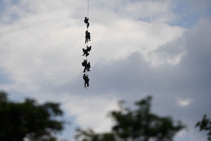 About nine police officers hang from a cable in the sky.