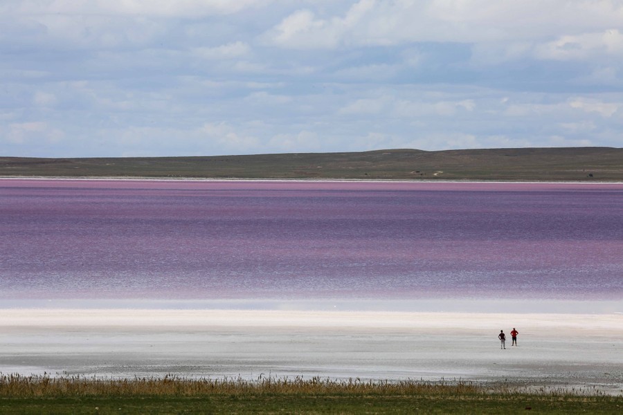 Two people stand on the shore of a colorful salt lake.