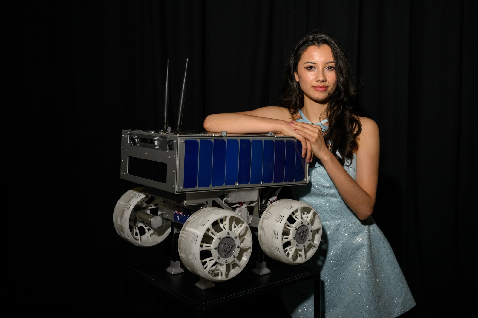 A person poses, leaning on a small lunar rover.