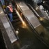 A man in a construction vest stands on a flooded escalator in a subway station.