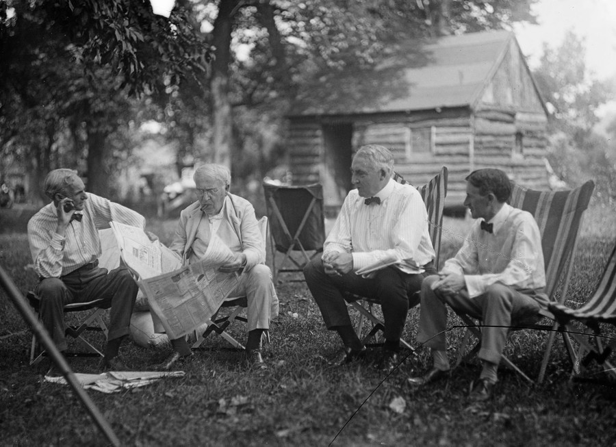 Four men sit together in lawn chairs outside a cabin.