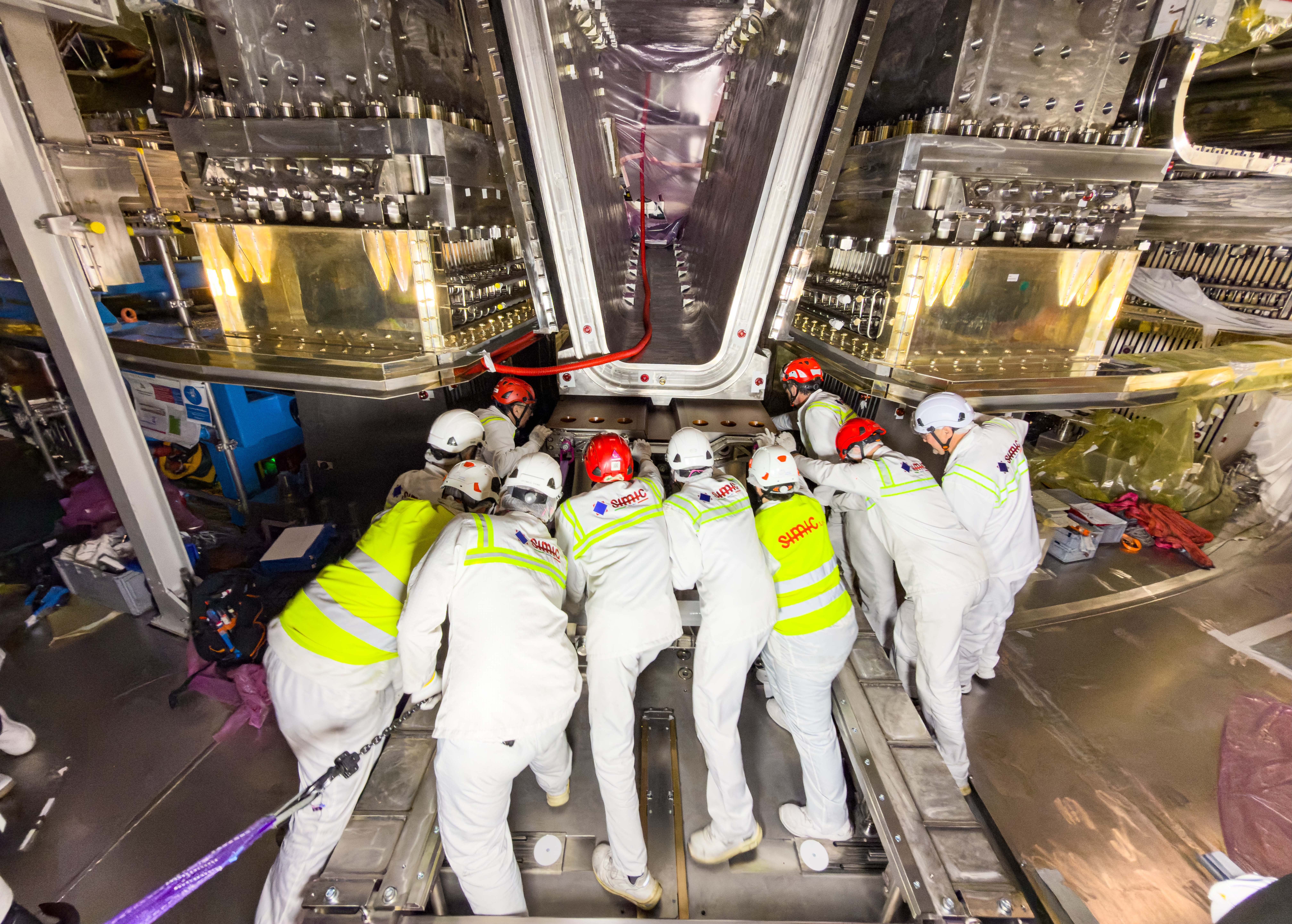 Ten workers move together to push a large component into place beneath a fusion reactor.