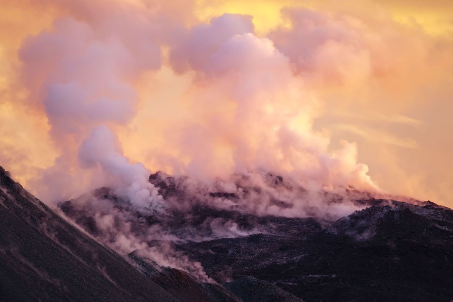 Steam rises from a volcano, seen at sunset.