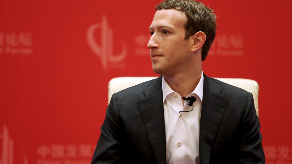 Mark Zuckerberg sits on a chair against a red background.