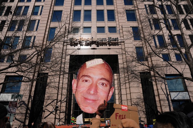photo of rally with Washington Post building in background and large cardboard protest sign with Jeff Bezos's face on it