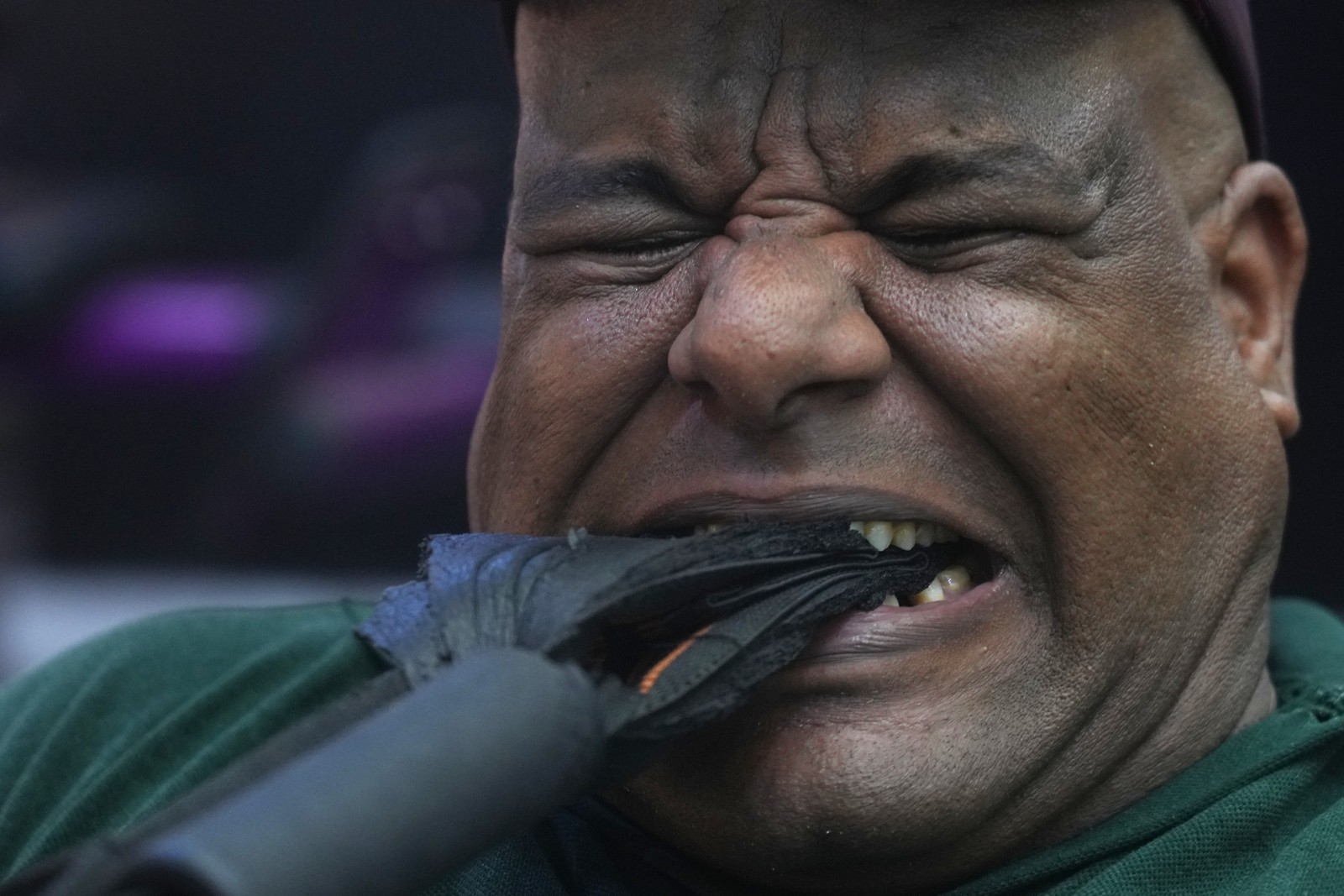 A strongman grimaces as he pulls on a cloth handle attached to a weight, using his teeth.