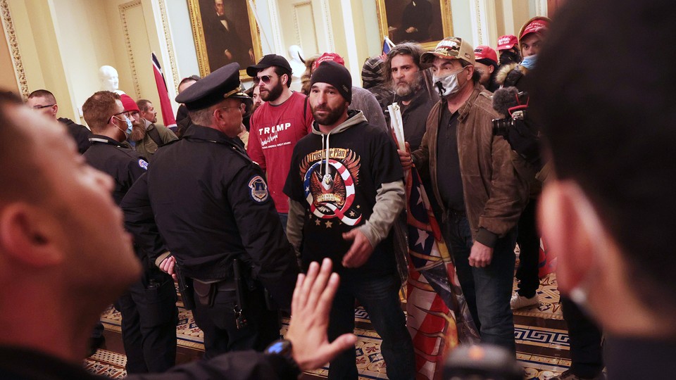 Insurrectionists inside the Capitol building, confronted by police. Man in center is wearing a QAnon T-shirt.