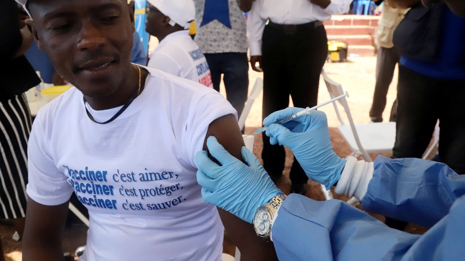 A person wearing blue gloves administers a vaccine to a man wearing a white shirt