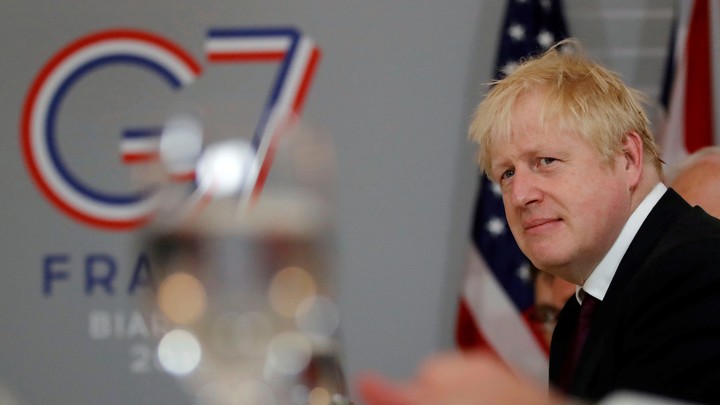 Boris Johnson stands in front of a sign for the G7 in Biarritz.