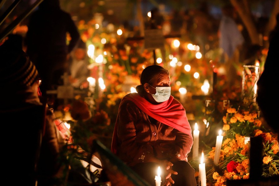 A person sits in a graveyard among many lit candles.