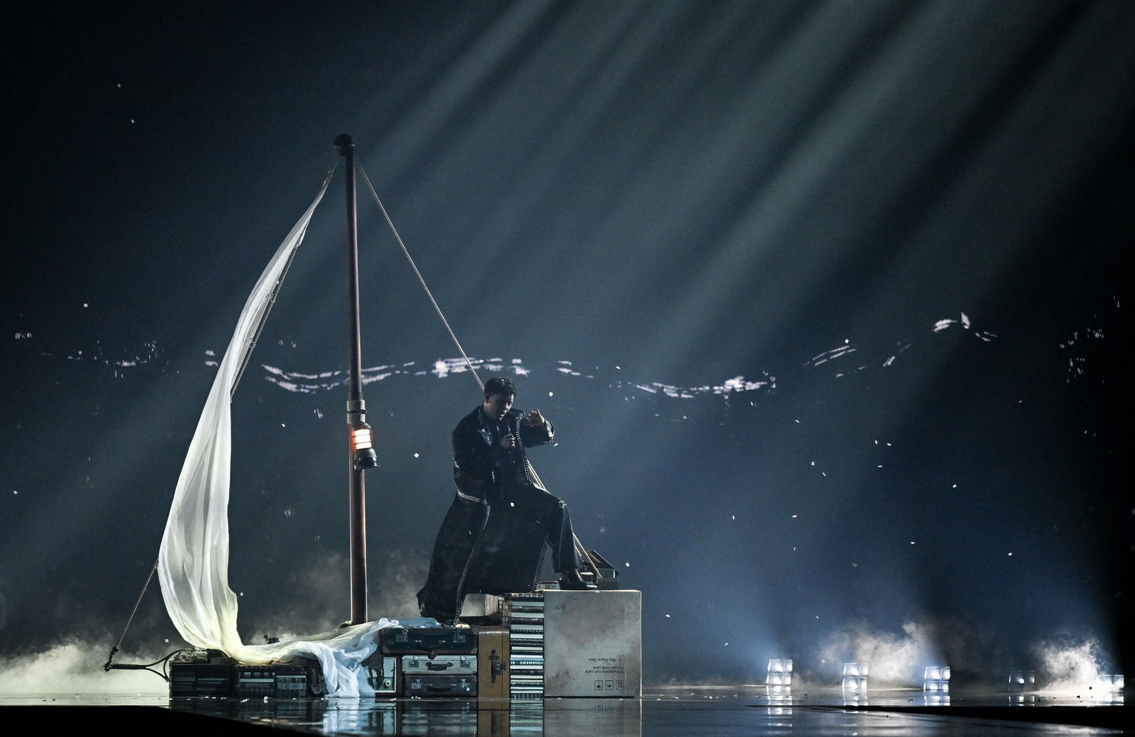 A performer sings while standing on set decorations that look like a sailboat made of cases and books.