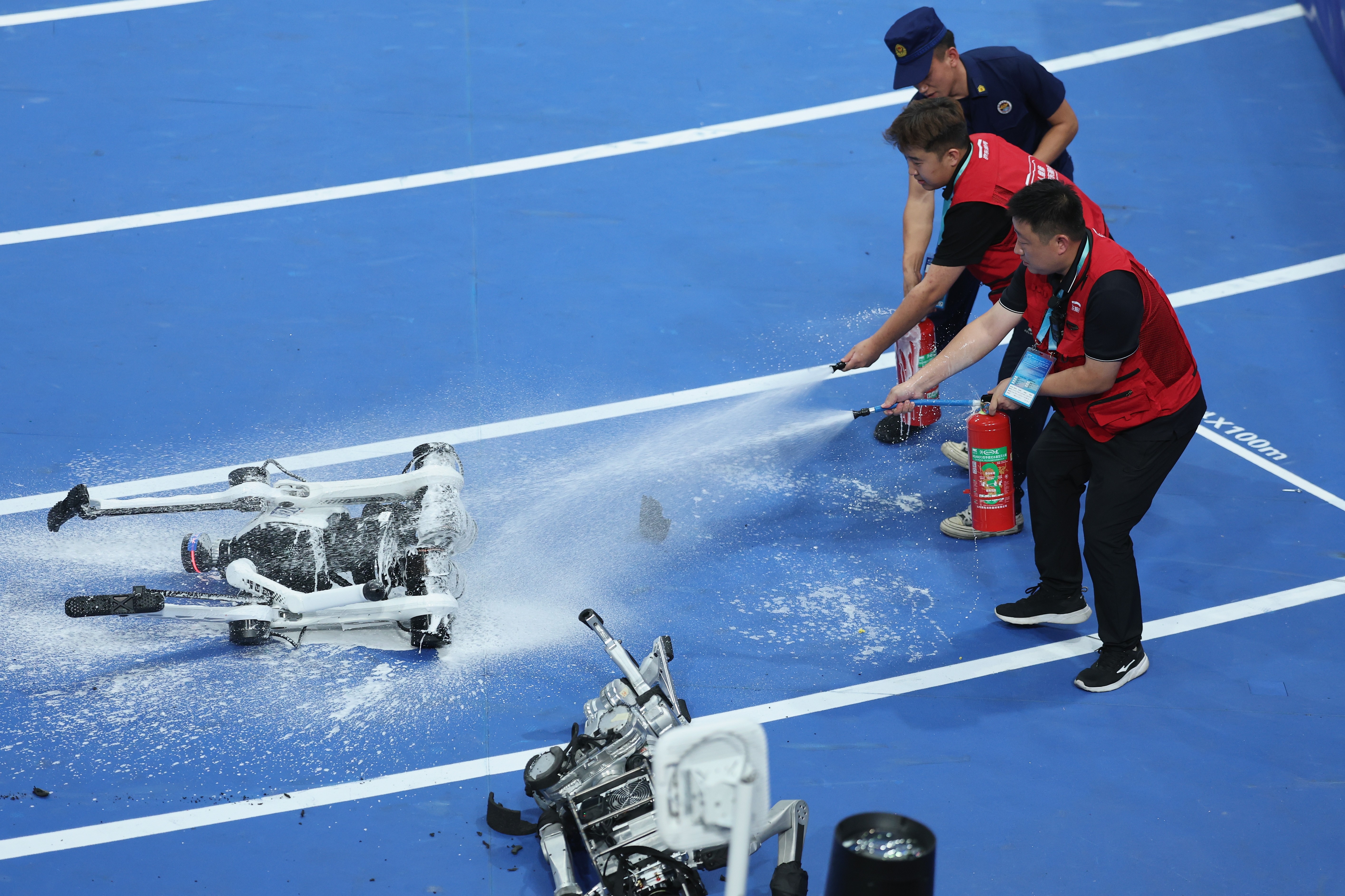Staff members douse a burning robot with fire extinguishers.