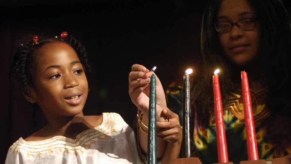A child and adult lighting the Kwanzaa kinara