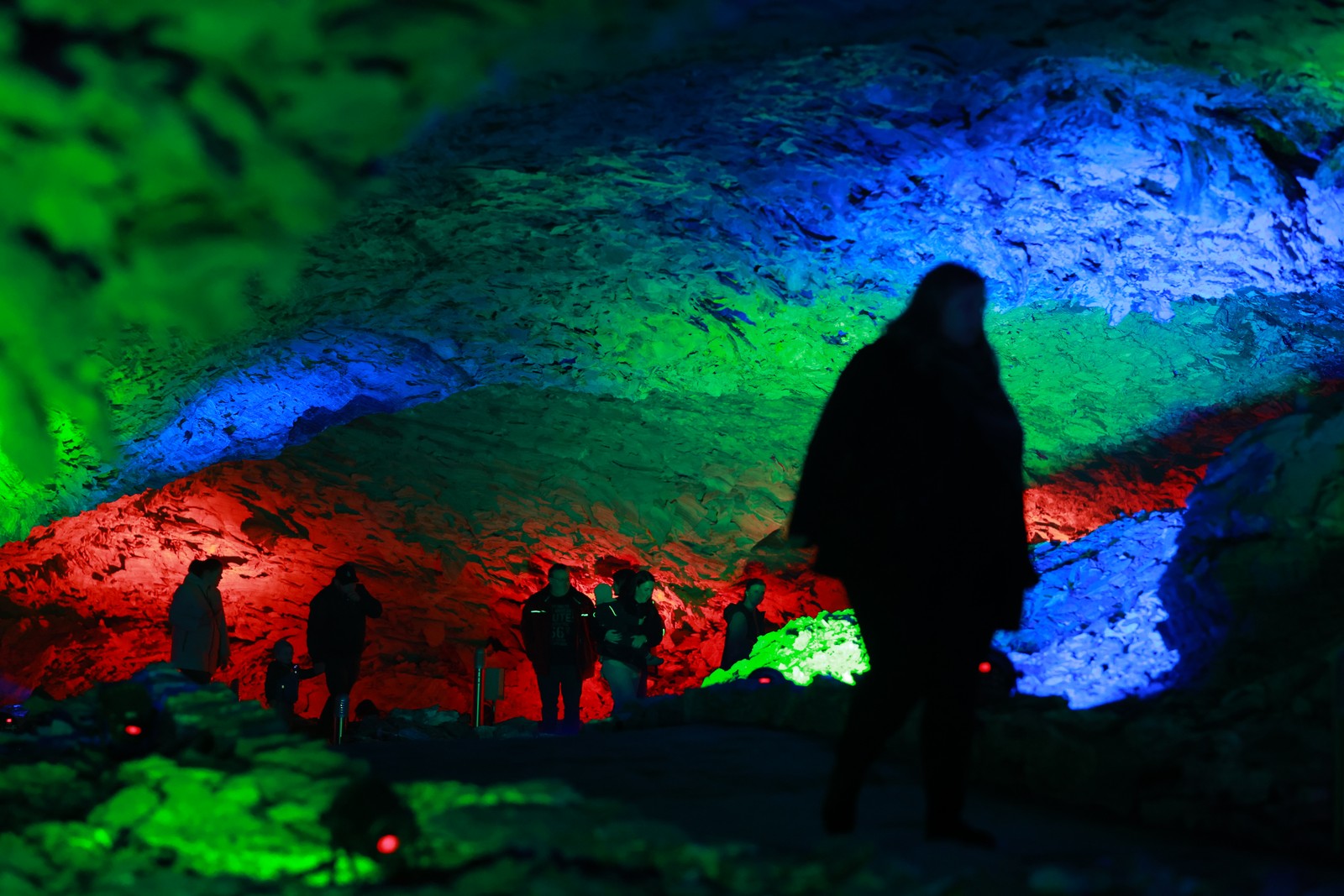 Visitors walk through a cave that is illuminated by multi-colored lights.