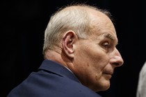 Former White House Chief of Staff John Kelly is seen in profile. The background behind him is black and he's wearing a navy suit.