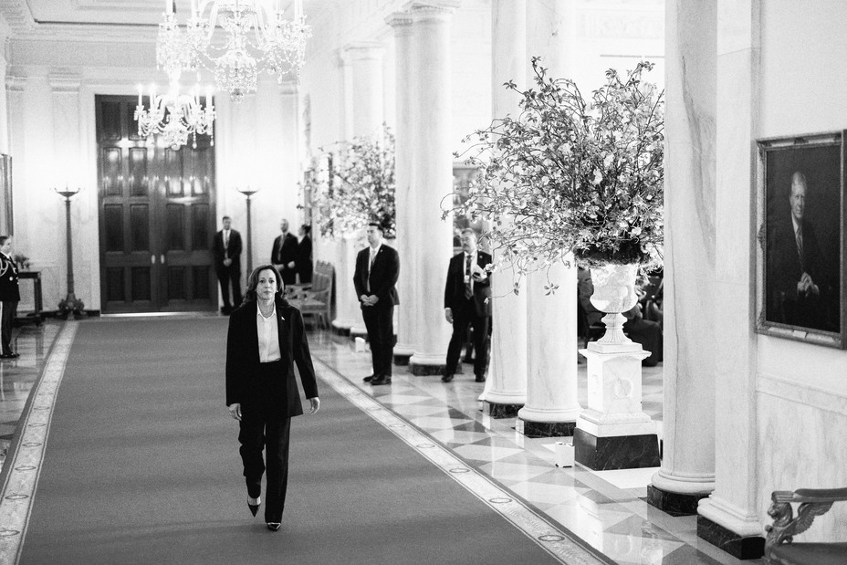 Black and white image of Kamala Harris walking in the White House while Secret Service members look at her in the background
