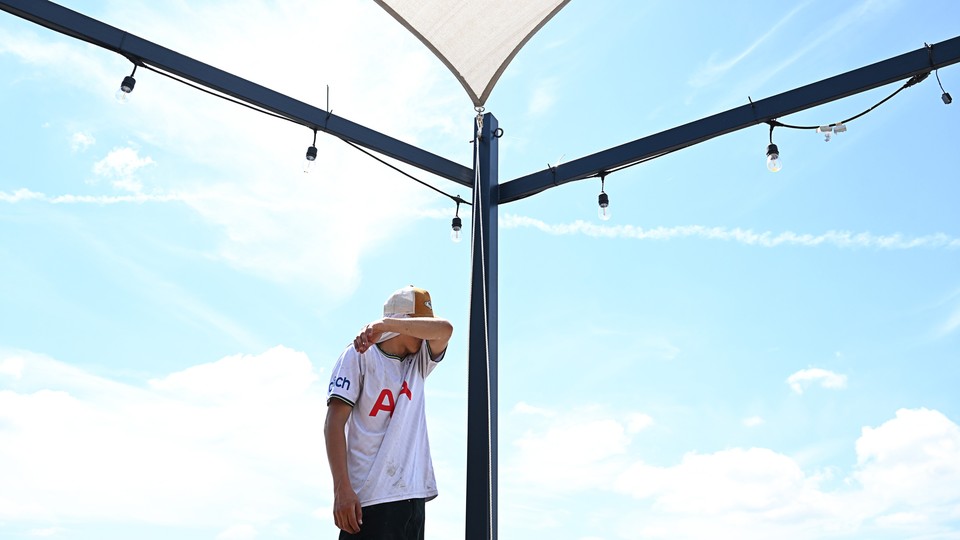 A man wipes his forehead under the hot sun as he walks under shade sail.