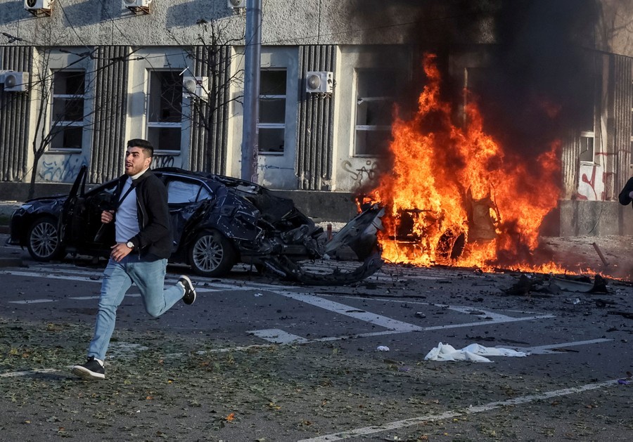 A person runs from smashed and burning cars after a missile strike on a city street.