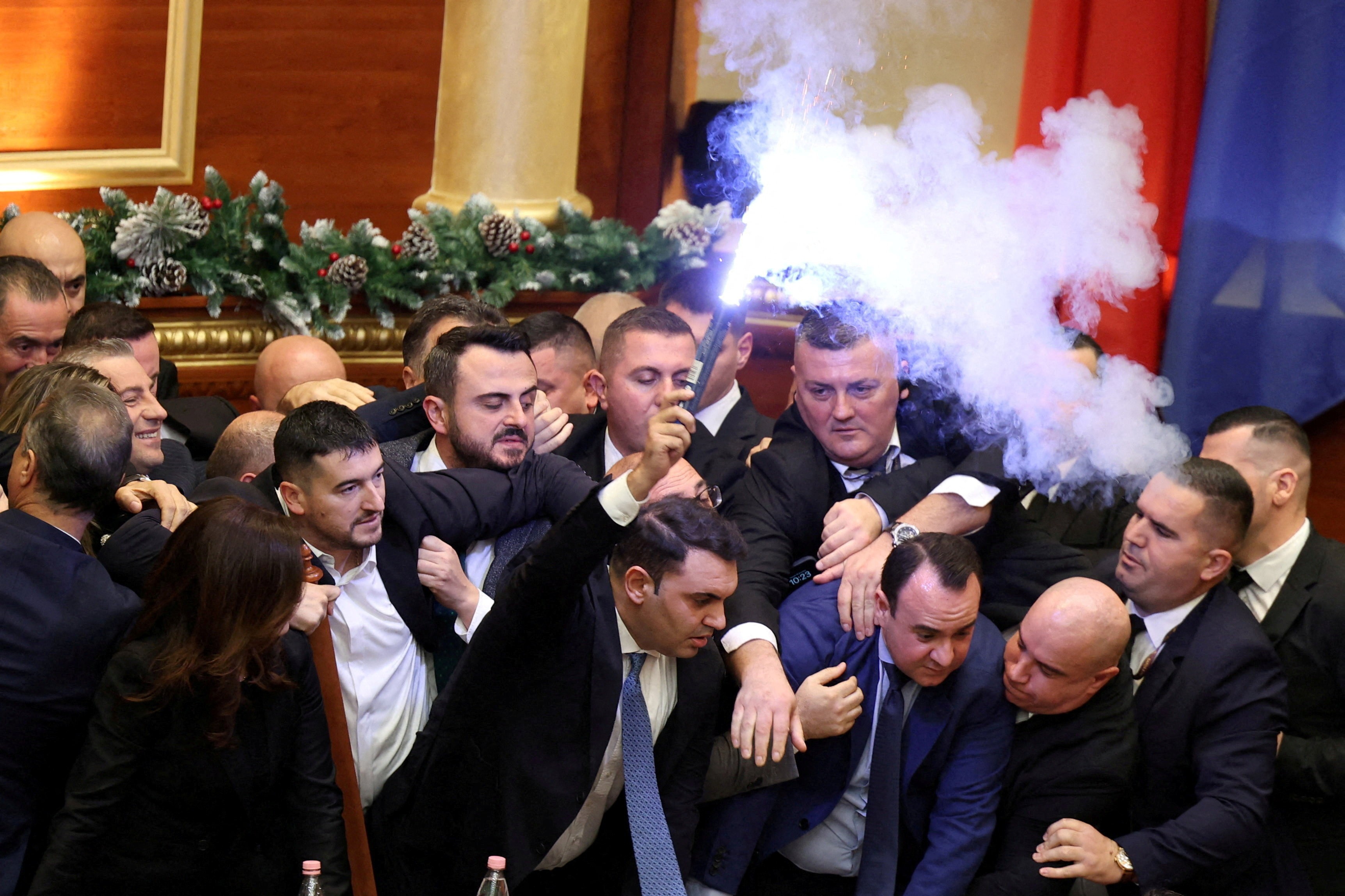 Members of Parliament in Albania scuffle inside a government building, one holding up a lit flare.