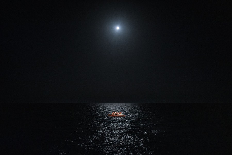 A single, small boat is seen in a large ocean at night, backlit by the moon.