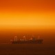 A large ship travels across a stretch of ocean that appears red in the sunlight