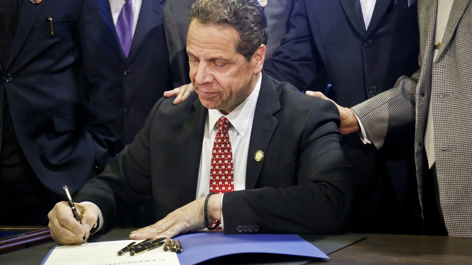 Andrew Cuomo signs a bill. There are six other pens he does not appear to be using but that stand at the ready should the ink run dry.