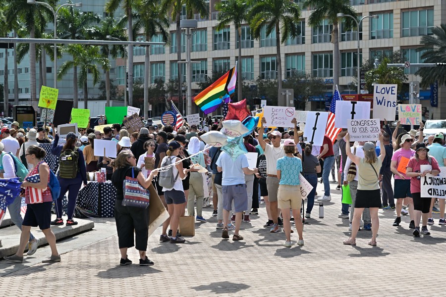 A group of protesters hold signs and flags outside a building.