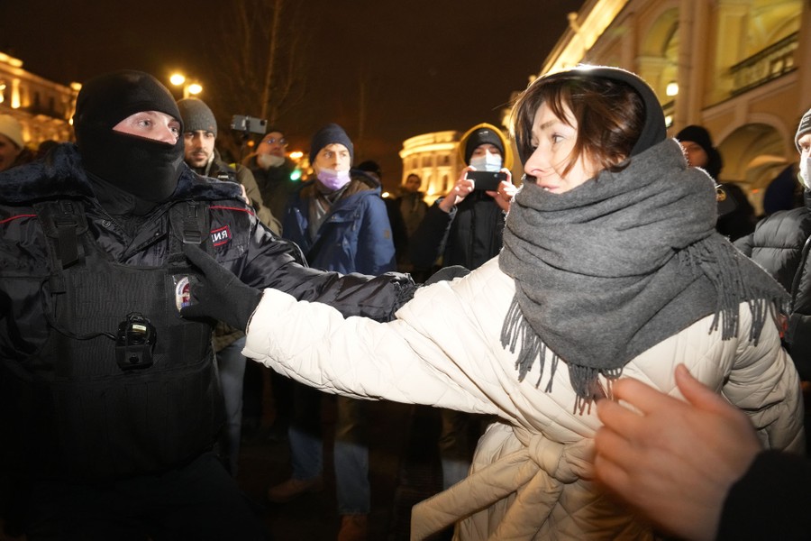 A police officer detains a woman, pulling on her arm.