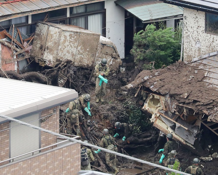 Soldiers search among debris piled up in a street among houses.