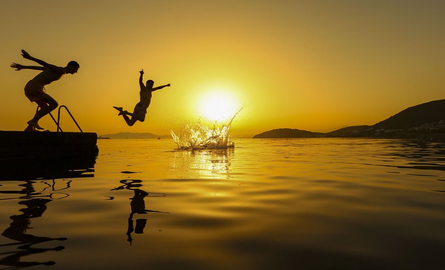 Several men jump from a dock into the sea at sunrise.