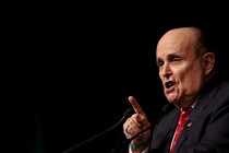 A close-up of Rudy Giuliani speaking on a stage in front of a black backdrop