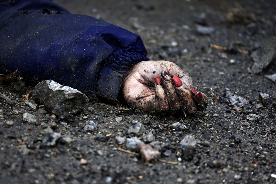 A woman's hand sticks out of a jacket sleeve, covered in dirt, on a rubble-strewn street