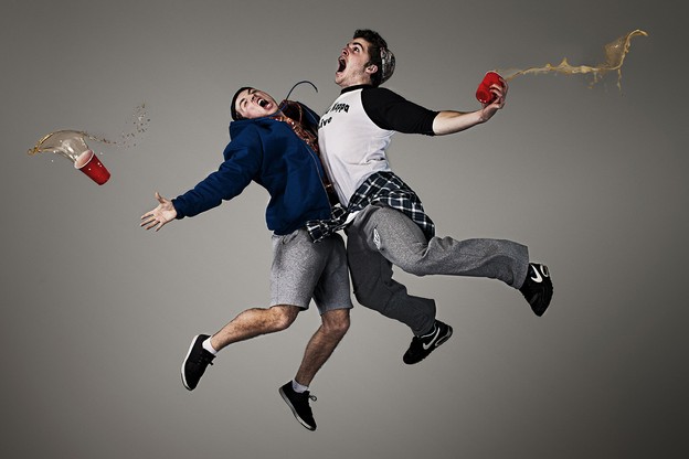 Two shouting white young men collide in midair, holding red plastic cups