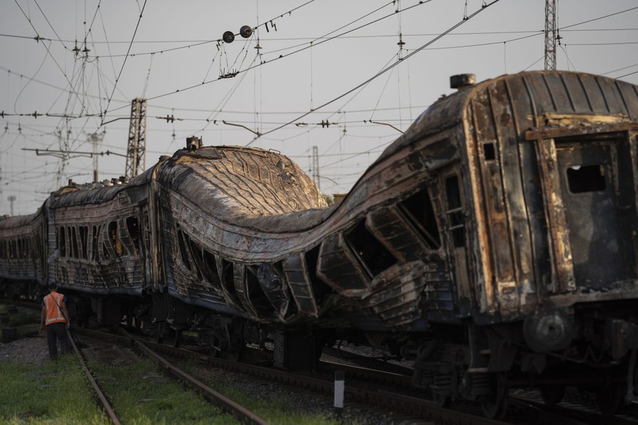 A person stands beside rail cars that have been smashed and burned.