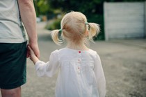 A little girl with pigtails holds an adult's hand.