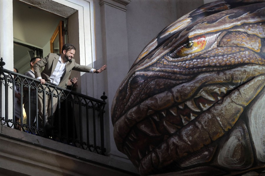 A man leans out of a balcony to touch the head of a large inflatable dinosaur.